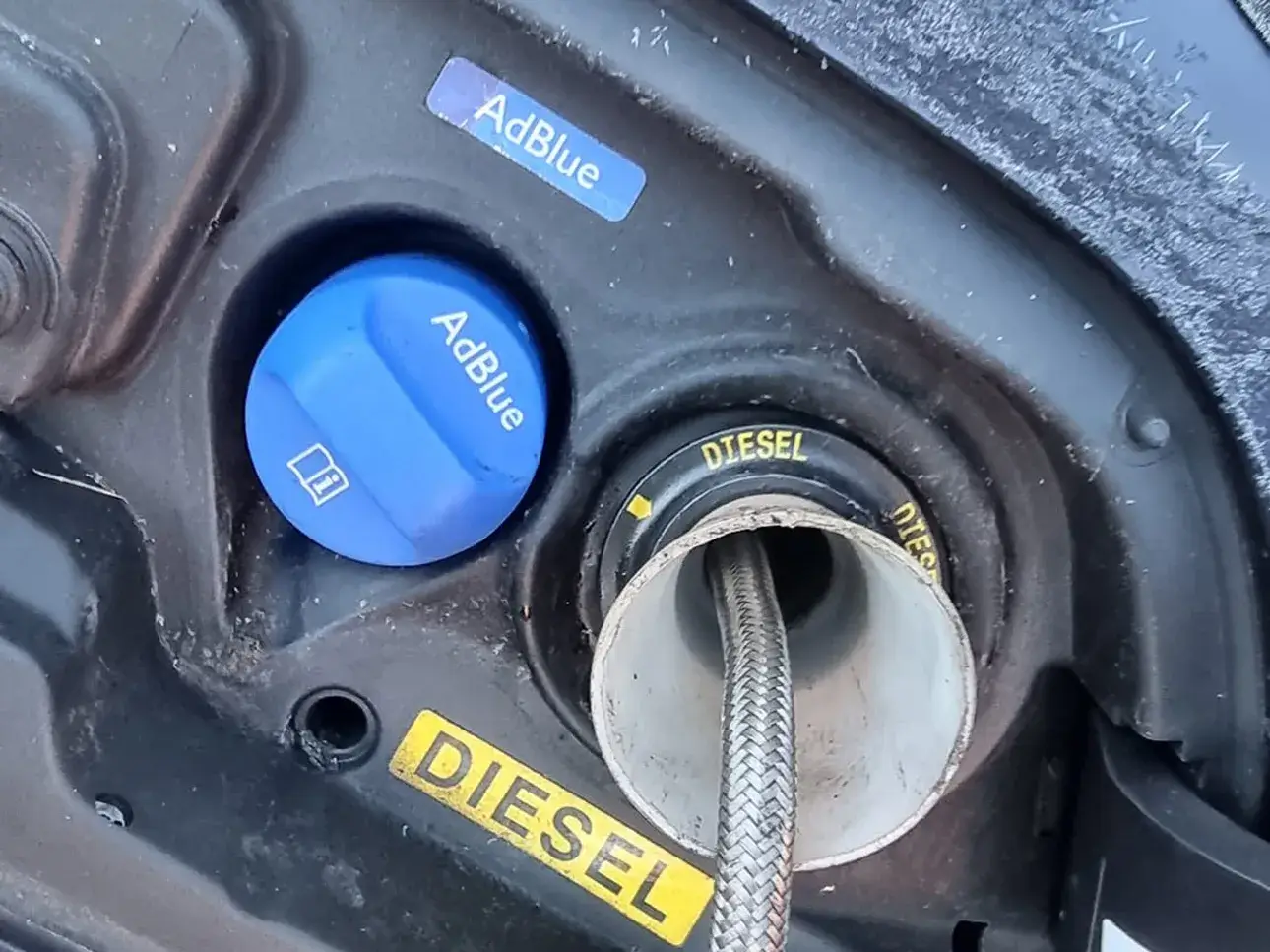 Fuel drain equipment connected at a vehicle fuel filler beside the AdBlue cap.